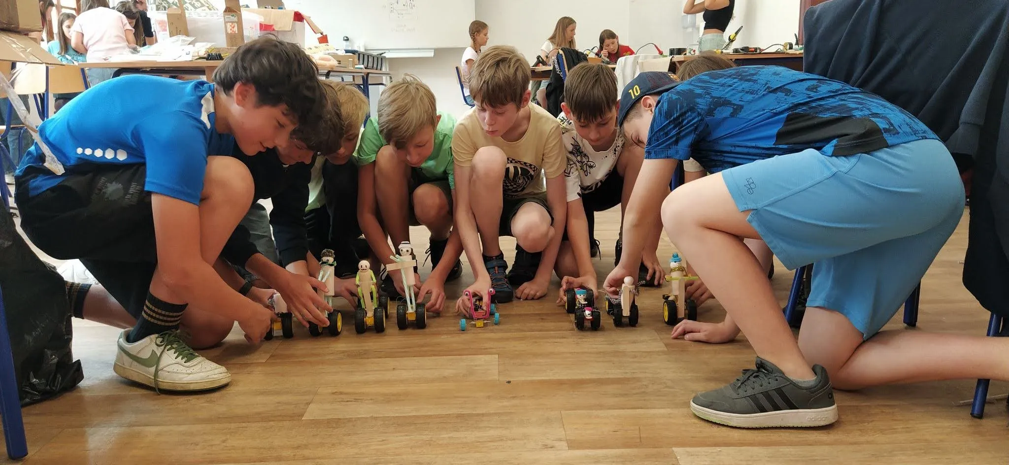 Skupinka dětí sleduje závod vlastnoručně postavených robotů